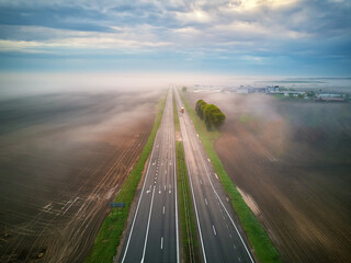 Aerial view of a highway covered by fog. Early misty morning. Road in rainy spring summer fields.