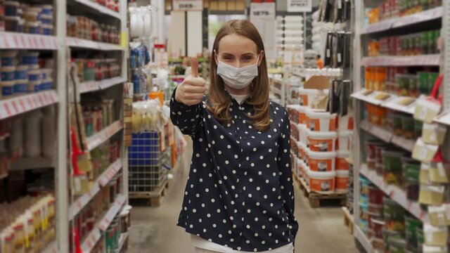 Woman wearing a protective mask shows the thumbs up in a hardware store