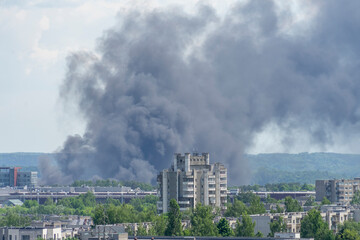 Fire in the city. Black column of smoke rises to the sky over city buildings