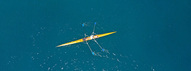 Aerial drone ultra wide photo of fit women athletes rowing in sport canoe in deep blue Aegean sea,...