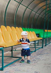 Portrait of a cheerful boy on a summer day. Beautiful child in a baseball cap at the stadium near the bright seats.