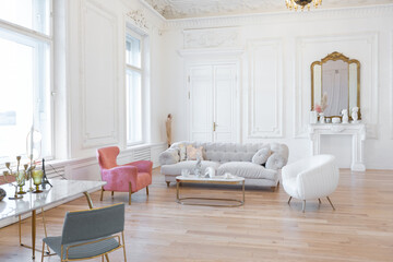very light baroque style luxury interior of big sitting room. White walls decorated with awesome stucco. Royal style apartment with chic furniture with gold elements