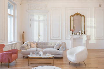 very light baroque style luxury interior of big sitting room. White walls decorated with awesome stucco. Royal style apartment with chic furniture with gold elements