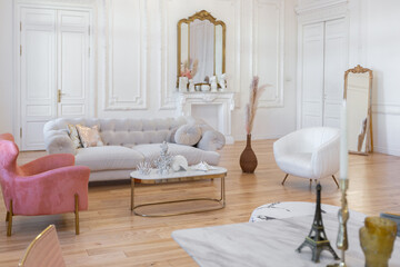 very light baroque style luxury interior of big sitting room. White walls decorated with awesome stucco. Royal style apartment with chic furniture with gold elements