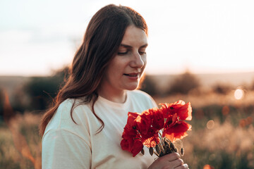 Beutiful young red-haired woman hand holding red poppies bouquet at sunset in the field