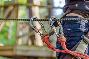 Forest Adventure Park. The woman fastens her carabiner and uses the climbing equipment. Overcome obstacles in the forest adventure park. Banner for advertising and place to insert text.