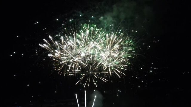 Celebratory fireworks in the night sky over the city, shot from a good angle from a drone, almost completely against a dark background.