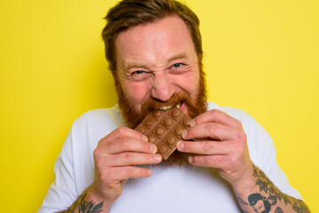 Happy man with beard and tattoos eats chocolate