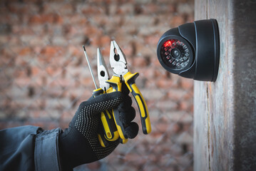 Security camera on the wall close up and worker hand with a work tools. Video surveillance system...