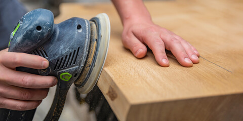 A carpenter works in a workshop. Joiner's grinders, furniture manufacturing. A carpenter is grinding a wooden part with an electric sander. place to insert text