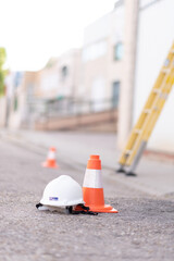 cone and safety helmet on the ground with yellow ladder in the background