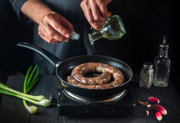 Chef adds oil to pan with raw homemade meat sausage. Preparation for cooking sausages in the kitchen of a restaurant or cafe on table with vegetables
