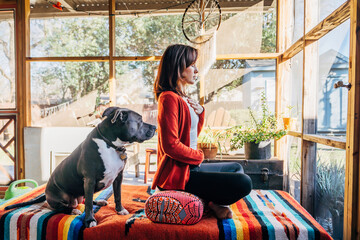 Woman meditating with eyes closed on sunlight filled porch with Pitbull pet dog 