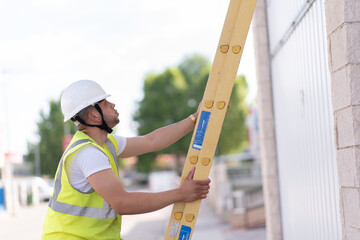 telecommunications technician coming down a yellow ladder and looking up, wearing a helmet and reflective vest.