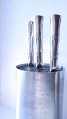 A set of kitchen knives in a metal block of knives with on a white background. Metal beautiful knife handles in a metal round knife block. Close up. Blue, white, silver color