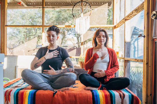 Women sitting and meditating together with hands on heart and stomach