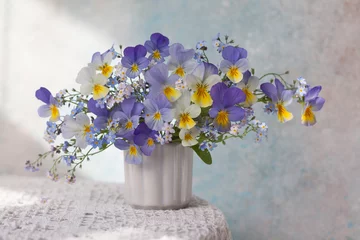 Deurstickers A bouquet of pansies and forget-me-not flowers in a vase on the table. Blur, selective focus. © tachinskamarina