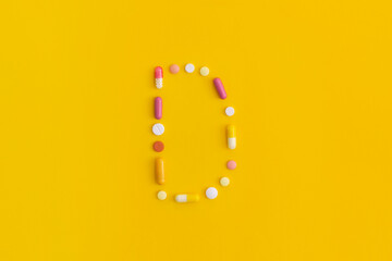 Vitamin D made from pills on yellow background. Top view with copy space. Flat lay.