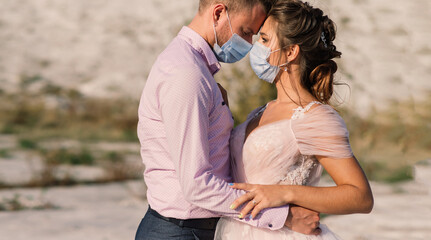 Young loving couple in medical masks in park during quarantine on wedding day.