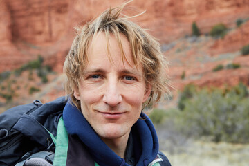 Backpacker, a young man with blond hair and blue eyes laughs at the camera. The mouth is closed....