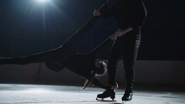 Pair figure skating on the rink. A man and a woman in a counter-light perform elements of the Olympic program together in slow motion