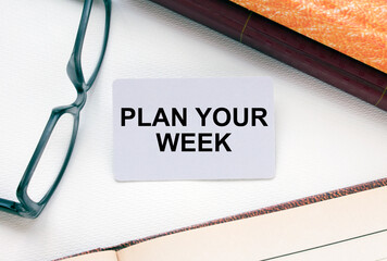 Text Plan Your Week on a business card lying next to notepad with eyeglasses and text documents