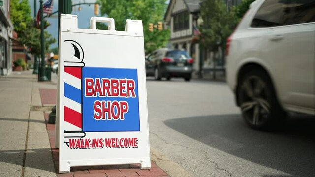 A sandwich board outside a small town's barber shop promotes the location as traffic passes by on the main street. Pittsburgh suburbs.  	