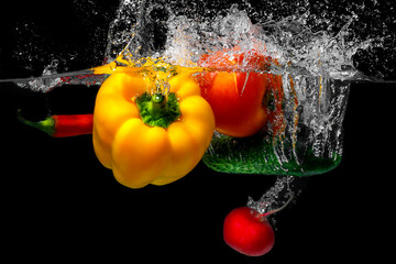 cucumber, radish, chilli, paprika, tomato in water with spray. Fresh vegetables splashing in water on black background