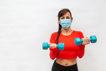 mulher fazendo exercício físico na máscara de proteção do corona vírus, com dois halteres em...