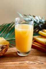 Pineapple juice. Glass of fresh natural pineapple juice on brown wooden table with ingredients. Fruit citrus orange fresh juice drink. Raw pineapple sliced fruit and palm leaves