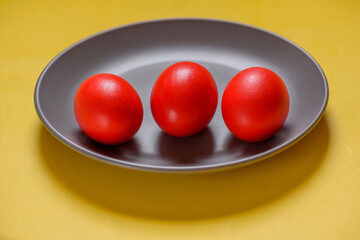 Red eggs, yellow background. Three eggs in a gray plate on a yellow background.