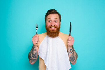 Happy man with tattoos is ready to eat with cutlery in hand