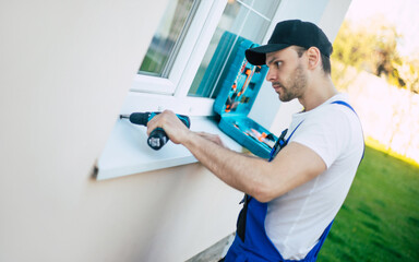 Side view photo of young workman in uniform while he installing or repairing window outdoors