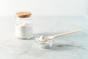 Eco friendly natural cleaners, jar with baking soda, lemon and wooden spoon on marble table background. Organic ingredients for homemade cleaning. Zero waste concept.