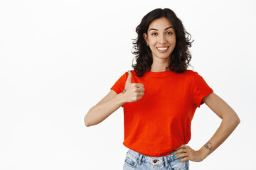 Supportive girlfriend shows thumb up, smiles and looks proud, satisfied with good results, praise...