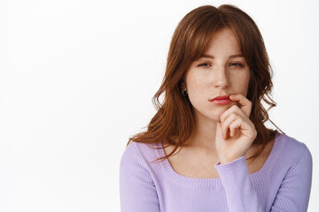 Close up of thoughtful or suspicious young woman, squinting with disbelief, staring at camera and pondering, thinking or making choice, standing over white background