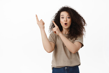 Surprised brunette woman showing interesting promotional text, pointing fingers at upper left...