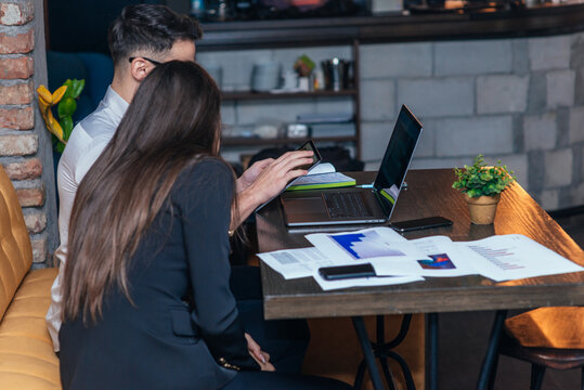 Sideview of a business meeting inside a cafe with two young colleagues sitting at a table, sharing some new ideas and looking at their laptops