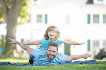 Fototapeta premium Happy man father and boy child pretend flying relaxing on blanket summer outdoors, enjoyment