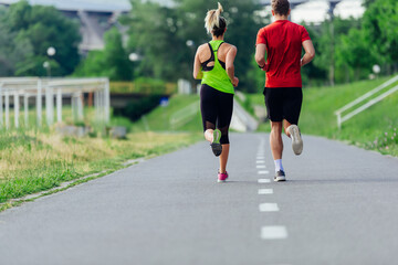 Obraz premium Rearview of caucasian female and male running outdoors on a road