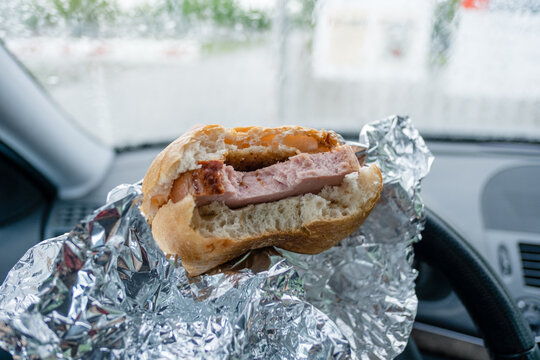 Man Eating Meat Sandwich In Car Waiting In Front Of Gate