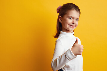 Optimistic girl kid showing thumbs up against bright yellow background