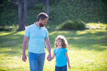 Fototapeta premium parent leads little child boy on lawn grass. dad with kid boy on summer day.