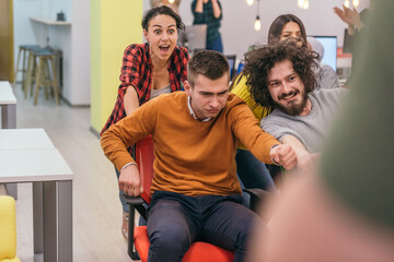 Team building and office fun.Four young cheerful businesspeople in smart casual wear having fun while racing on office chairs and smiling..