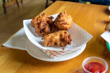 Fried Clam Cakes at a Rhode Island restaurant served in a paper basket on wooden table with condiments