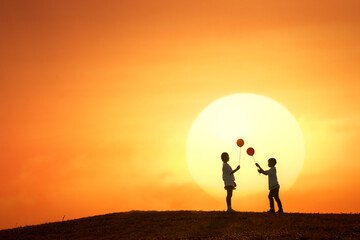 Silhouette of boy and girl holding balloon witn sun background
