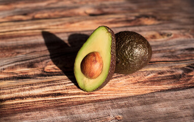 cut ripe avocado lies on a wooden table under the sun