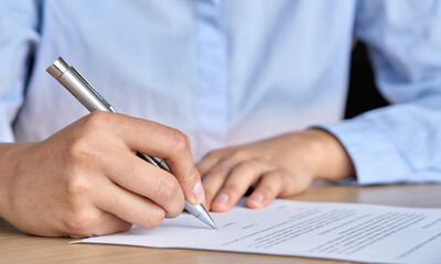 Closeup view of female corporation ceo business woman client hand signing putting signature on credit bank legal document, job contract, insurance agreement writing with pen on desk in office.
