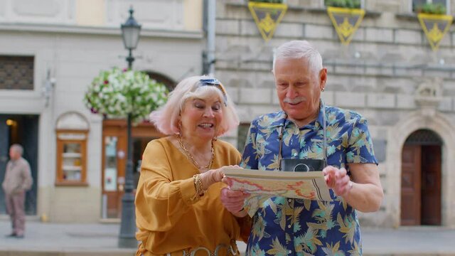 Senior couple grandmother and grandfather tourists in stylish clothing looking for a place to go in new city Lviv, Ukraine, using paper map. Elderly family man, woman on holidays vacation traveling