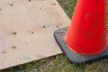 construction safety neon orange pylon or cone partly sitting on an old plywood board on grass - construction site theme